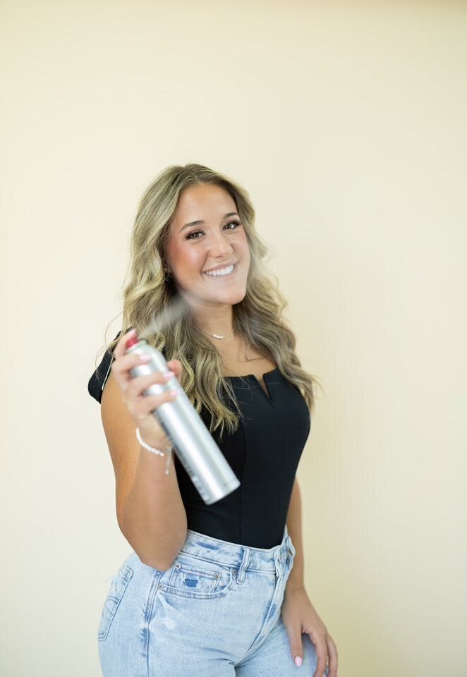 Kylie Cupp smiling and spraying hairspray toward the camera